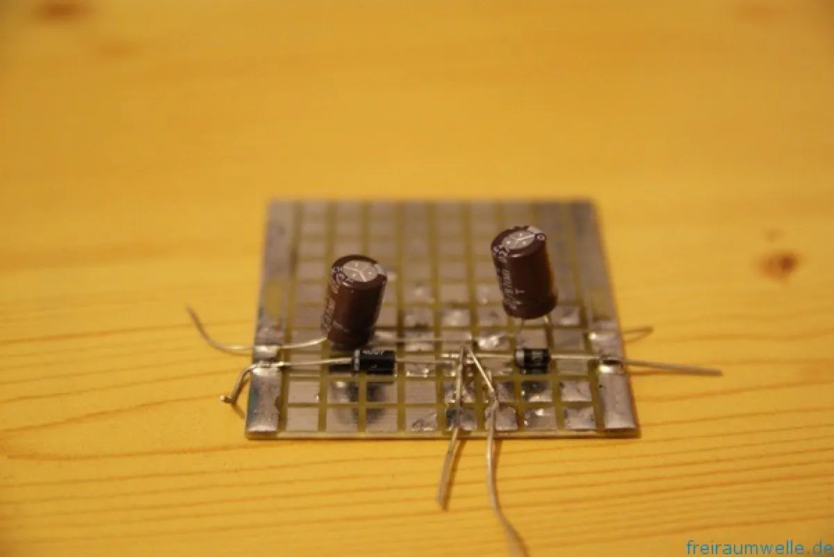 Kleine Lochrasterplatine mit zwei stehenden Elektrolytkondensatoren und zwei liegenden Dioden, die Anschlussdrähte stehen frei ab