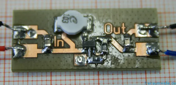 Kleine Platine auf Millimeterpapier, mit einer weißen Speicherdrossel, dem Wandler-IC in SMD-Bauform und den Beschriftungen In und Out auf der Kupferfläche