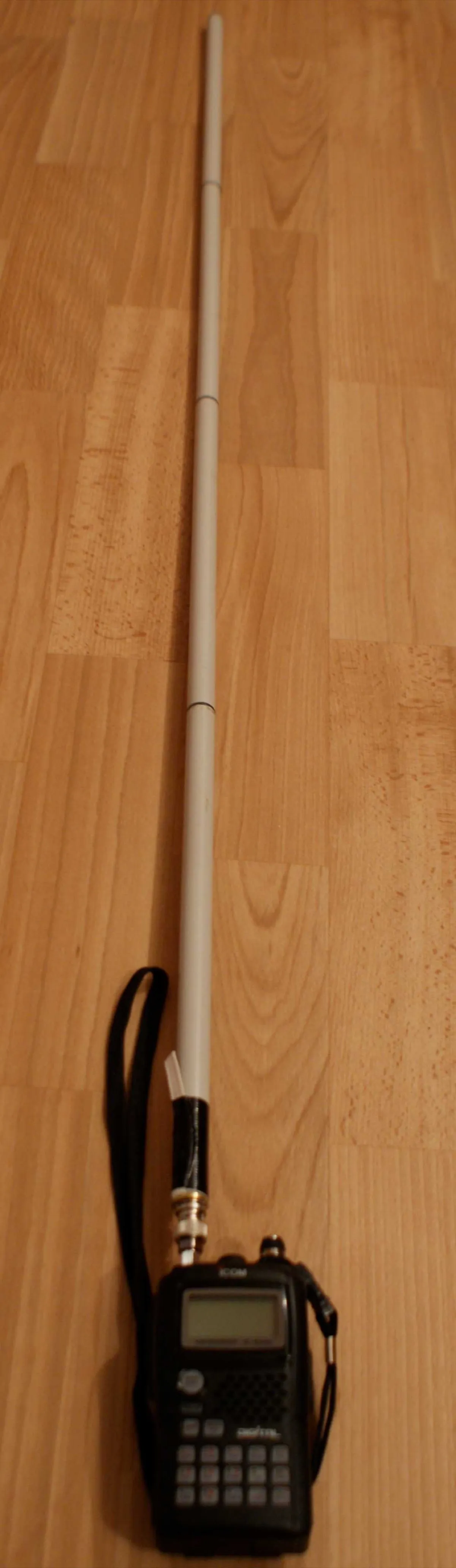 Ausgeklappte Antenne, an ein ICOM-Handfunkgerät geschraubt und auf einem Holzboden ausgelegt, deutlich länger als das Gerät selbst