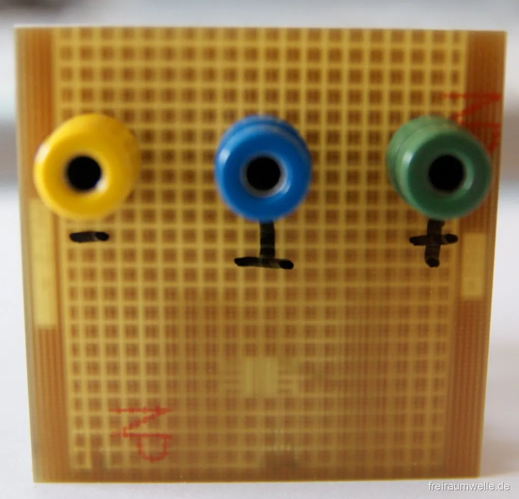 Rückseite der senkrechten Platine mit drei Bananenbuchsen in Gelb, Blau und Grün, jeweils mit den Beschriftungen Minus, Masse und Plus