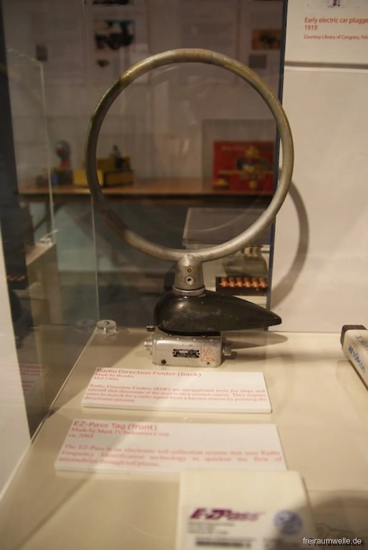 Vitrine mit einem Funkpeiler aus den 1930er Jahren: ein großer Metallring als Rahmenantenne auf einem gegossenen Sockel, davor die Beschriftungstafel