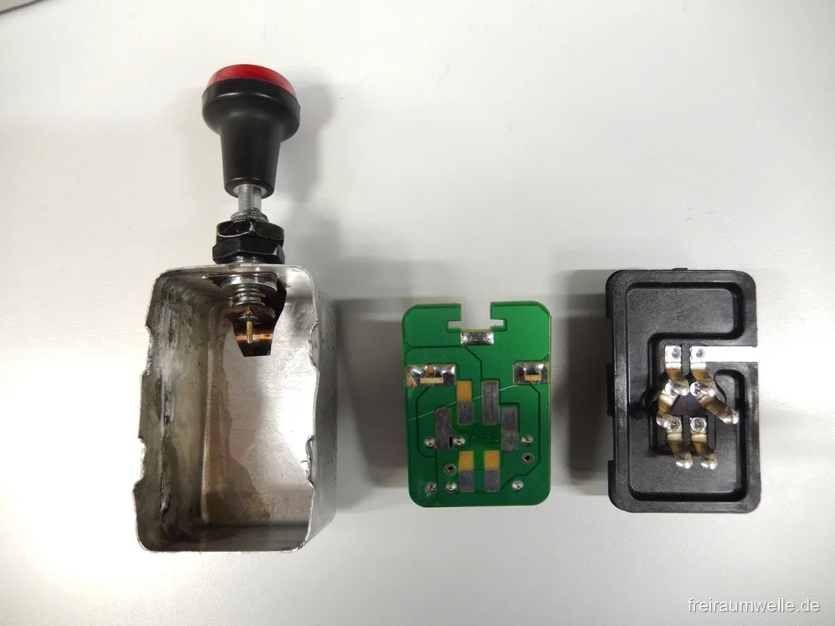Der zerlegte Warnblinklichtgeber in drei Teilen nebeneinander: Aluminiumgehäuse mit rotem Zugknopf, grüne Platine und schwarzer Kontaktträger